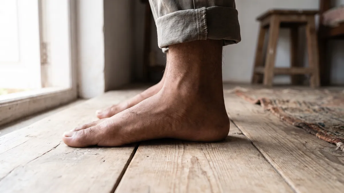 Bare feet standing on a wooden floor showing low, flat arches