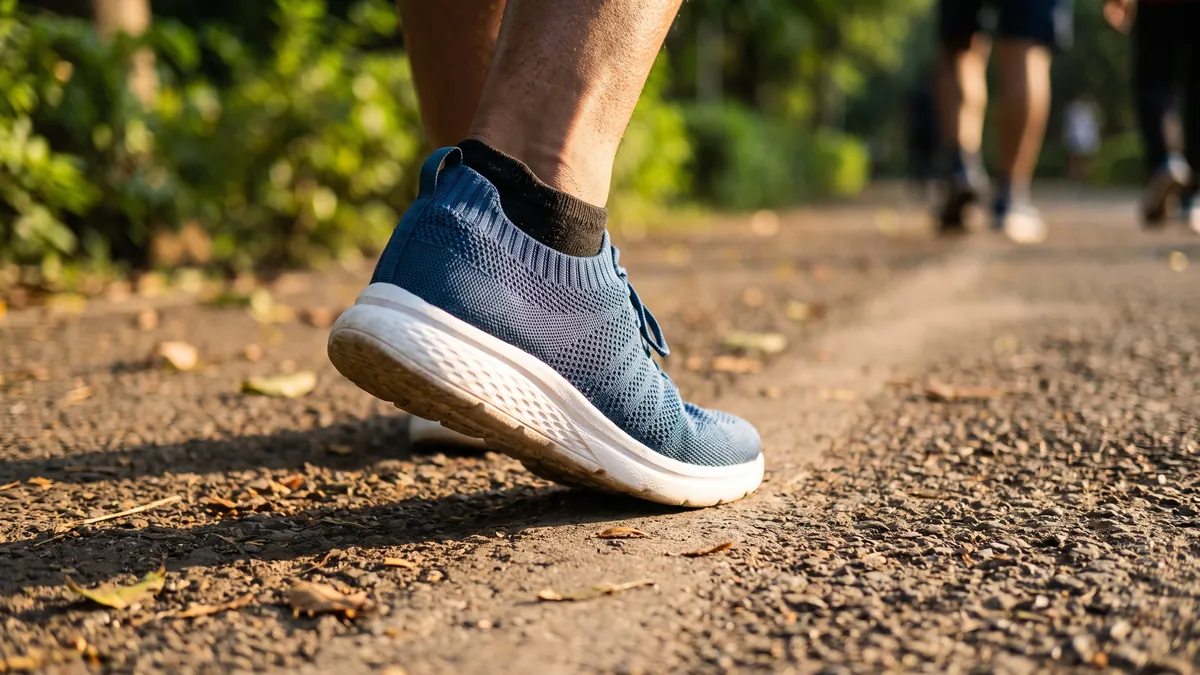 Foot in a lightweight blue knit walking shoe mid-stride on a park path