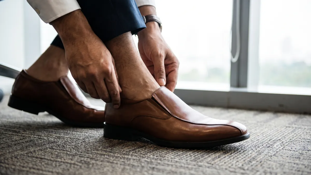 Man seated on an office chair sliding his foot into a brown leather slip-on formal shoe
