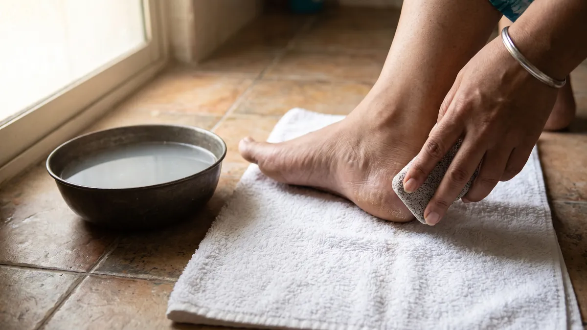 Woman gently smoothing a dry heel with a pumice stone after soaking