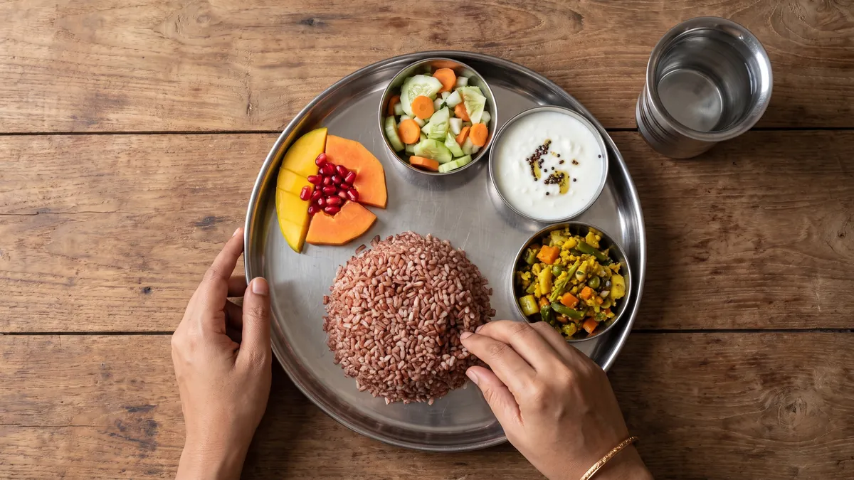 Healthy Indian meal with salad, curd, vegetables, red rice, fruit and a glass of water